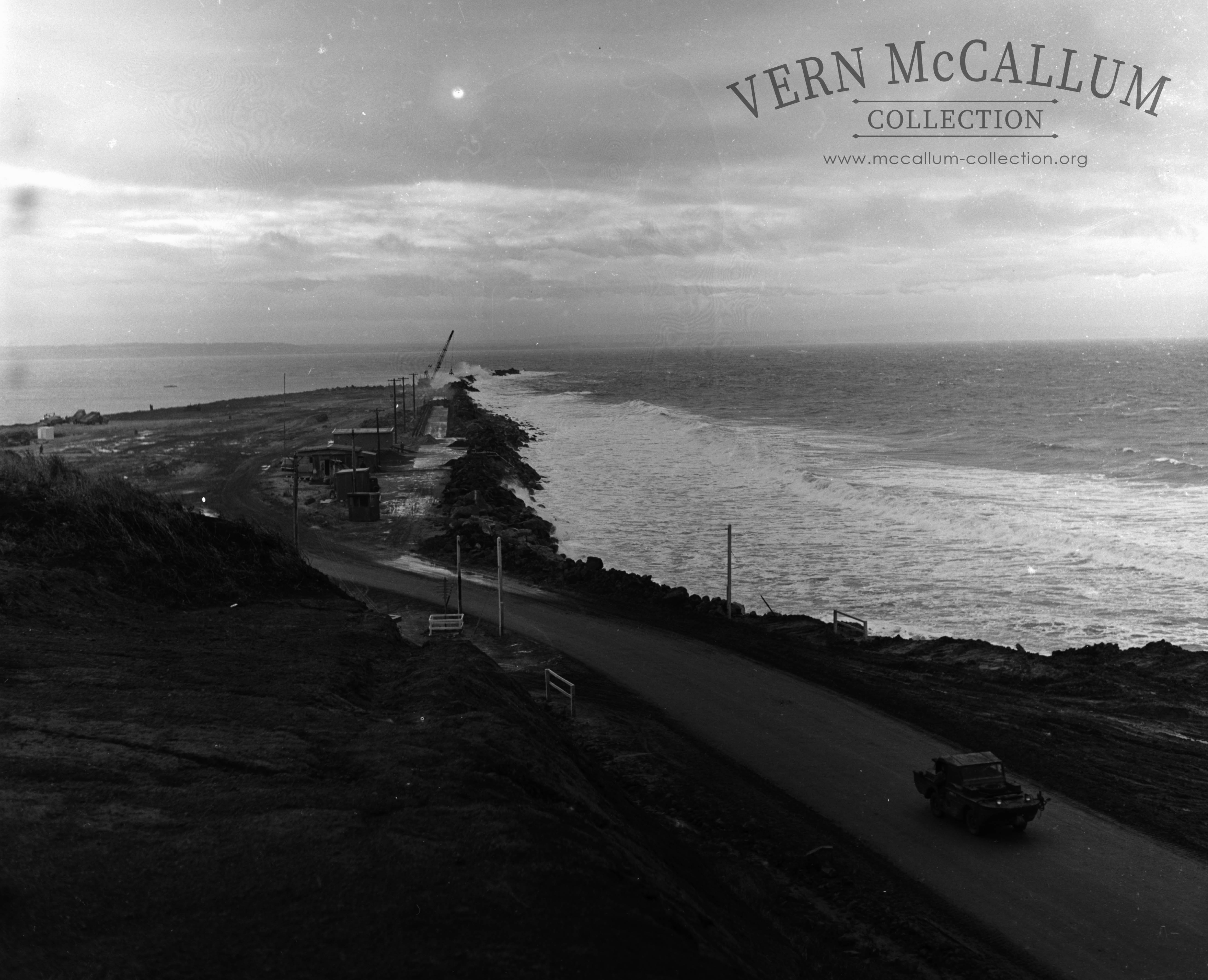 The main breakwater and quarry road during a heavy sea  note the army duck on the road this vehicle was used as a run around on the construction site.