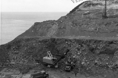 The Harman  excavator loading heavy rock at the quarry. Two bulldozers stripping overburden and pushing it into the sea in the top of the picture.
Building the port.
Photo courtesy Geoff Blackman.