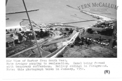 AERIAL VIEW OF THE HARBOUR FROM THE SOUTH WEST. NOTE THE DREDGER PUMPING TO RECLAMATION THE CANAL BEING FORMED WITH TEMPORARY COFFER DAMS RAILWAY SIDINGS IN THE FORE GROUND THIS PHOTO WAS TAKEN IN JAN 1958.  Photo courtesy Geoff Blackman.