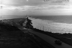 The main breakwater and quarry road during a heavy sea  note the army duck on the road this vehicle was used as a run around on the construction site.