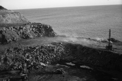 The quarry master drilling holes for blasting while rock is being carted to the harbour.